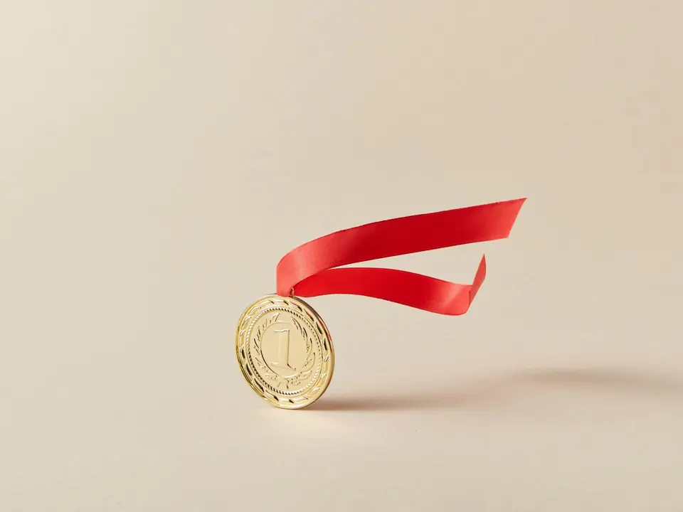 A gold medal with a red ribbon on a warm paper background