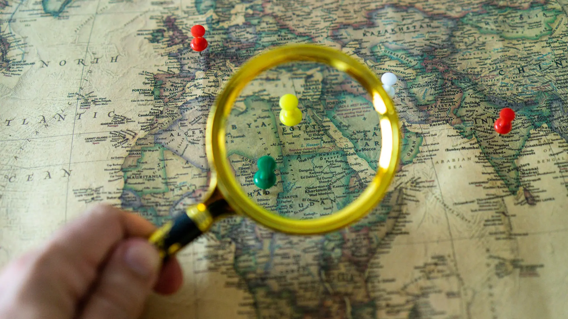 A magnifying glass held over a pinned wall map