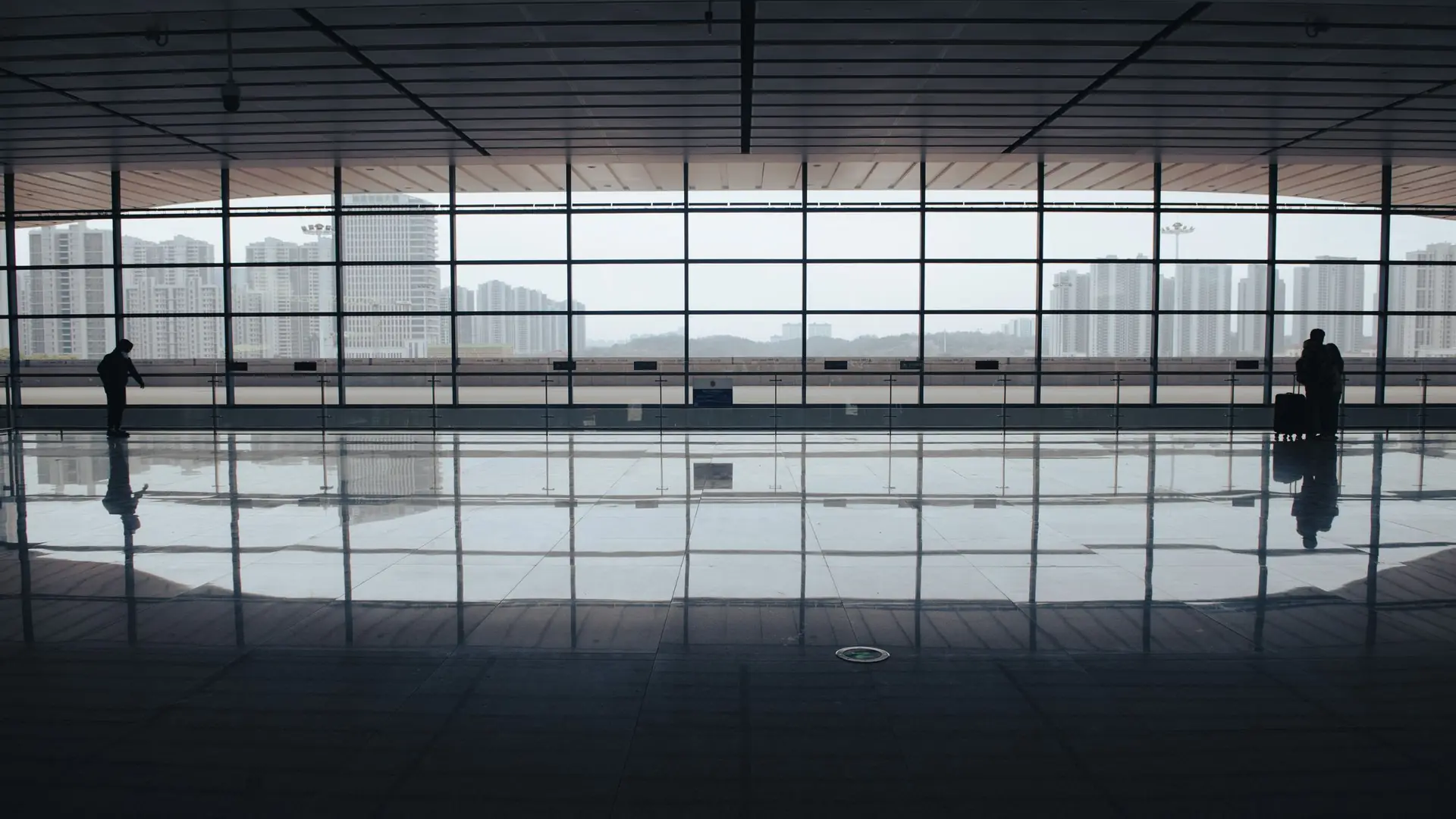 A lone traveller beside the tall windows of an airport terminal