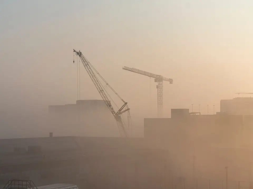 Construction cranes rising through soft morning mist