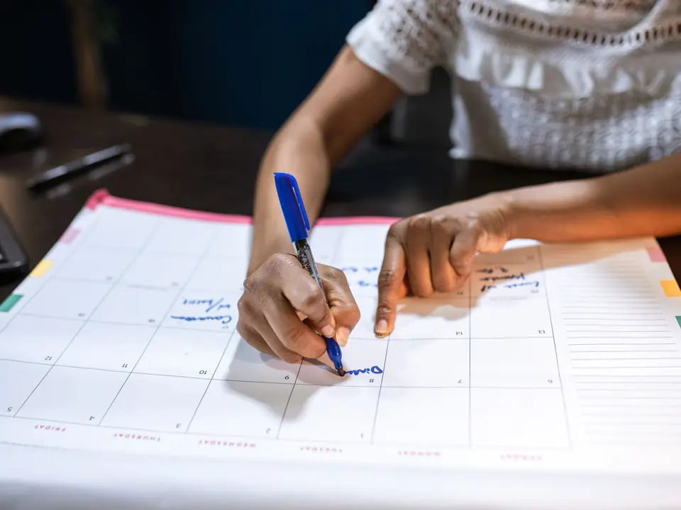 Hands writing an appointment into a large desk calendar