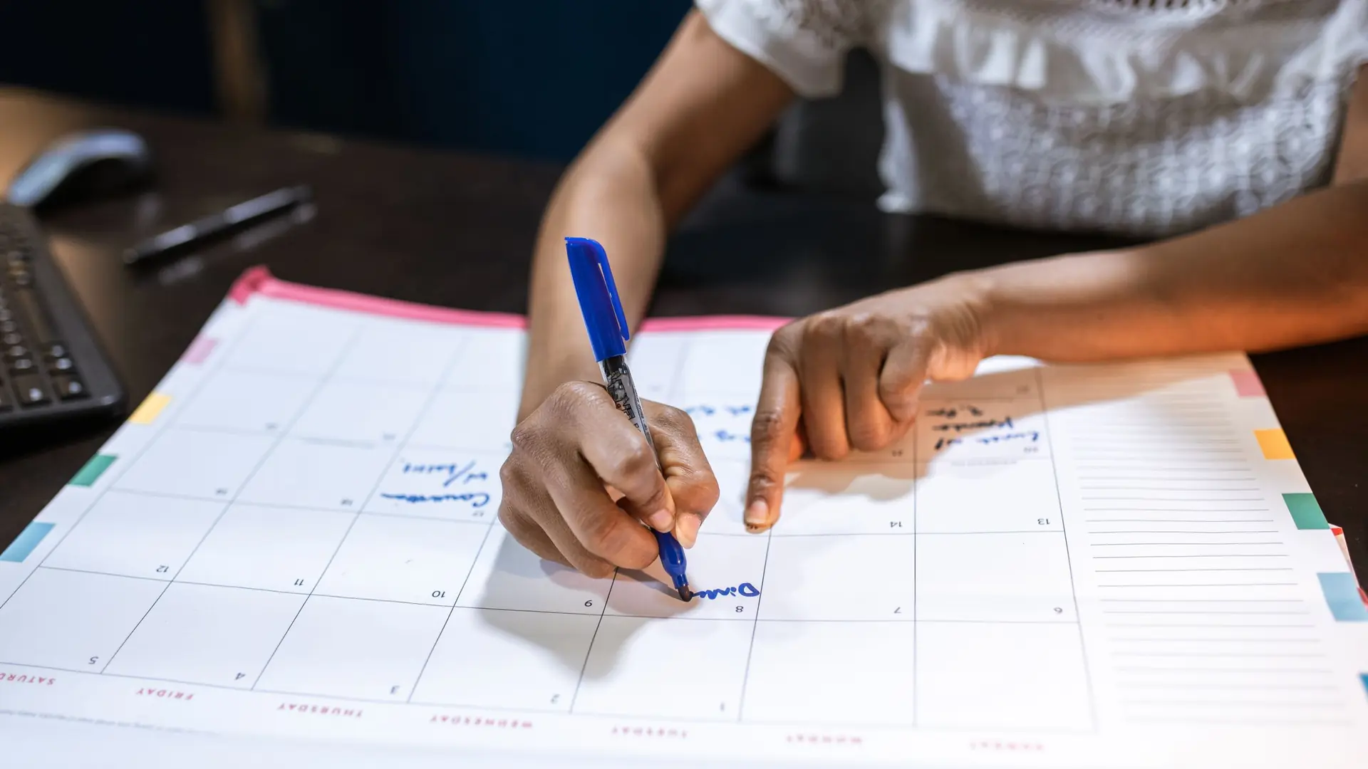 Hands writing an appointment into a large desk calendar