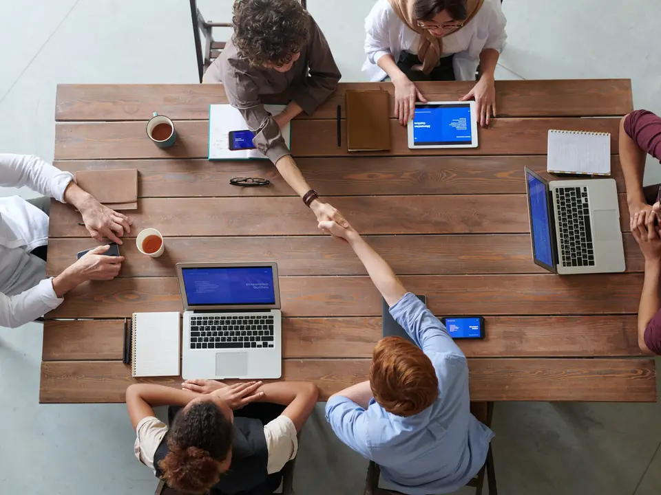 A team around a wooden table with laptops, seen from above